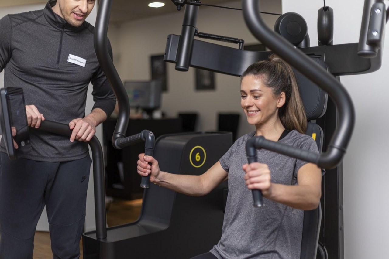 Therapeut betreut eine Patientin beim Training an einem medizinischen Trainingsgerät