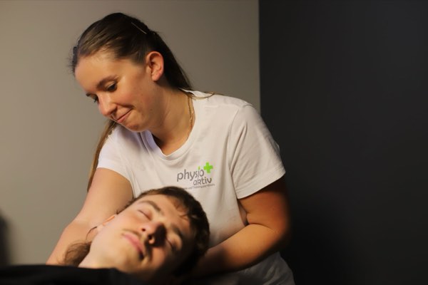 Physiotherapeutin stützt mit beiden Händen den Kopf eines entspannt liegenden Patienten