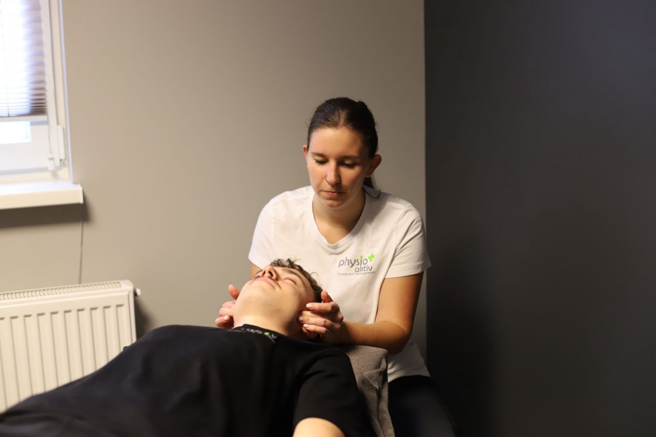 Physiotherapeutin behandelt mit beiden Händen die Halswirbelsäule eines liegenden Patienten