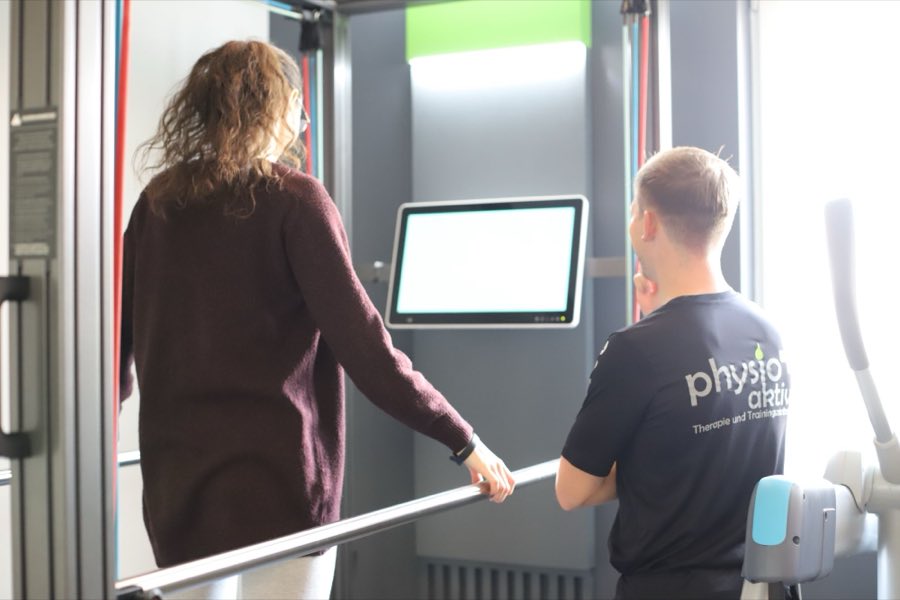 Therapeut begleitet eine Patientin beim Training an einem medizinischen Gerät